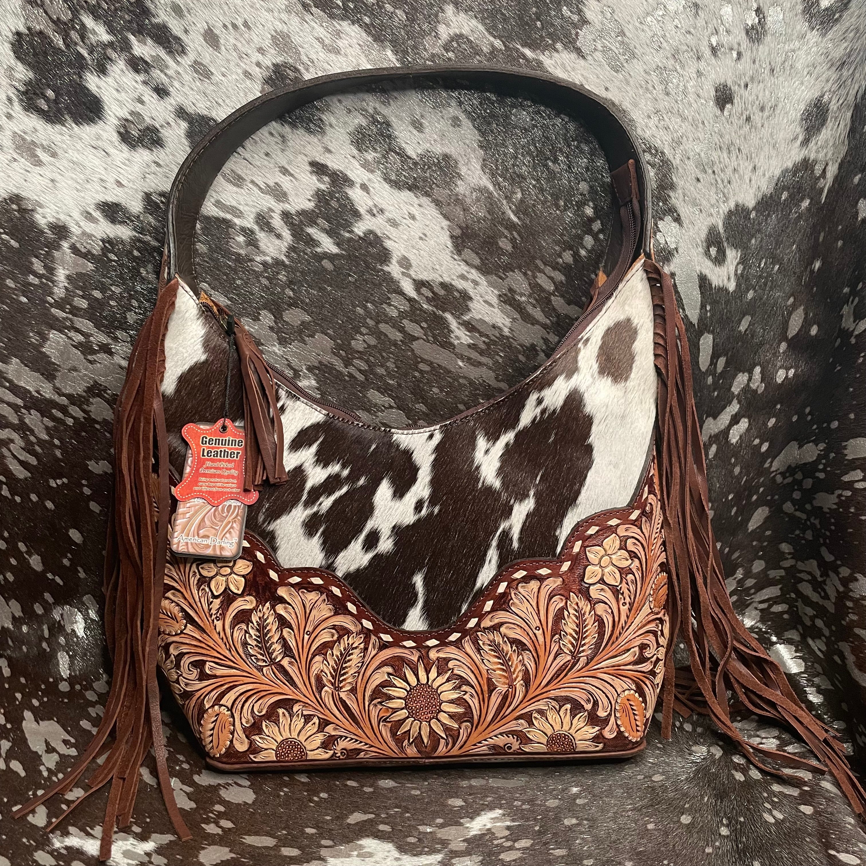 Cowhide leather handbag with floral tooled leather and fringe on a cowhide background
