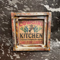 Decorative sign with 'Cowgirl Kitchen' text and graphics in a rustic frame on a textured surface.