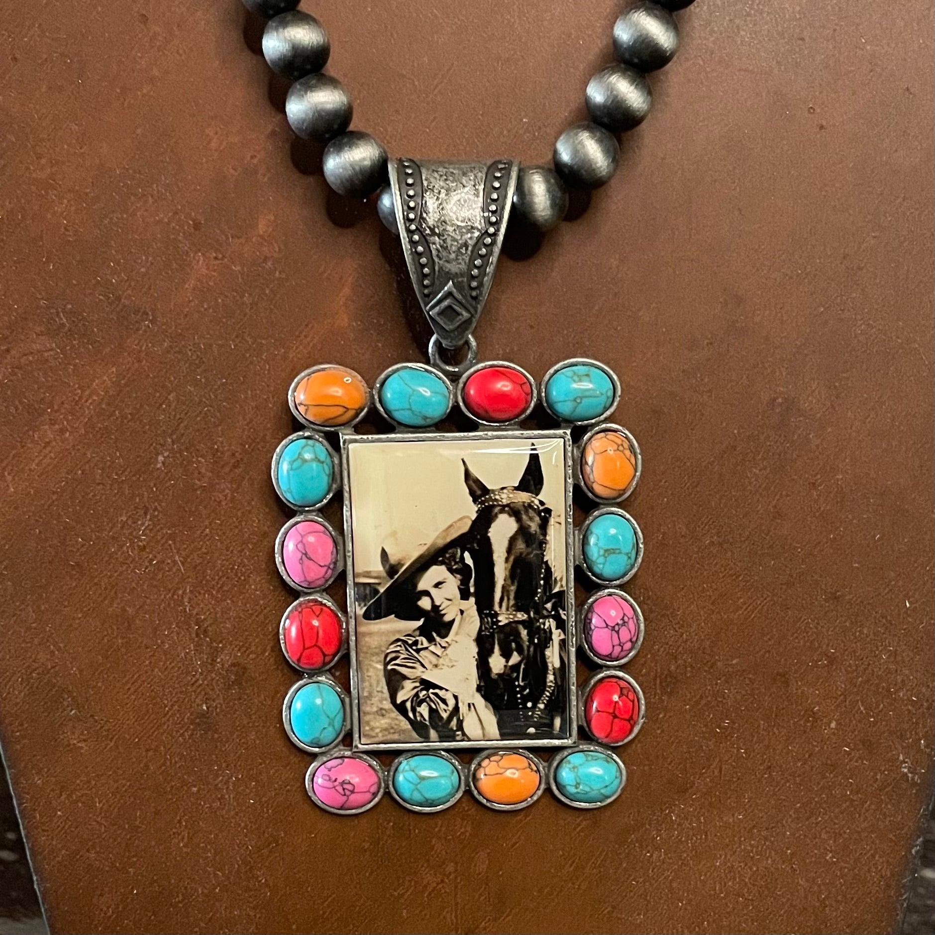 Necklace with pendant featuring a photo of a woman and horse, surrounded by colorful stones on a brown background.